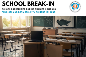 A photograph of a school classroom that has been broken into, showing damage and signs of theft. In the foreground, a wooden laptop trolley is open and empty, with a single black laptop sitting on top. Glass from a shattered window on the left side of the room is scattered across the floor, catching the light. Desks and chairs are disarranged, and a projector screen is torn. A chalkboard with some graffiti is visible in the background, completing the scene of a ransacked classroom.